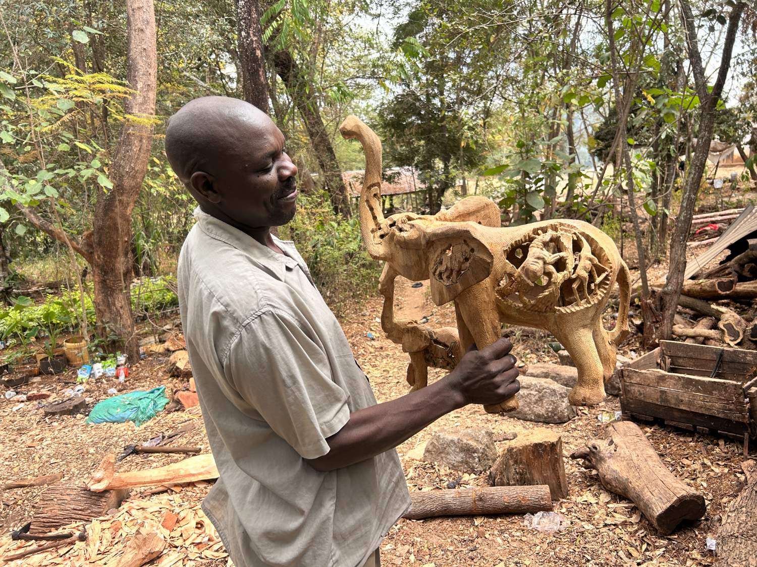 A carver holding a part finished elephant outside the carving sheds at Wamunyu