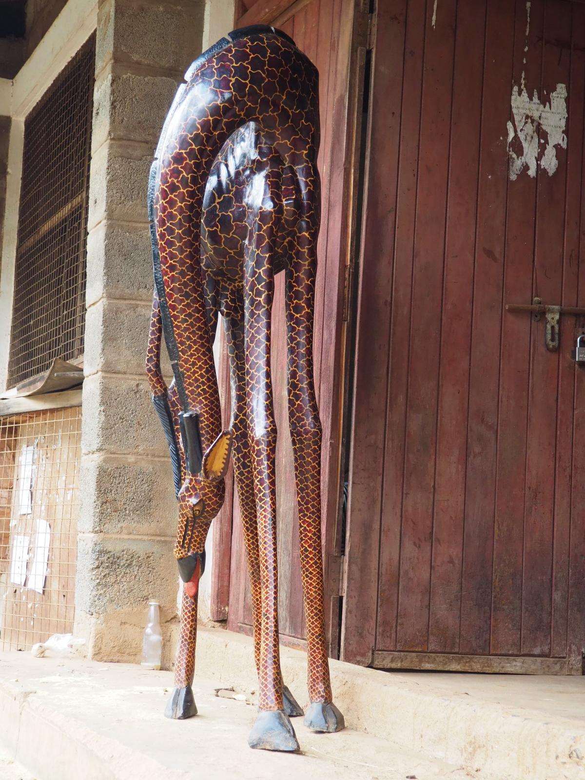 A tall carved giraffe standing against red timber doors