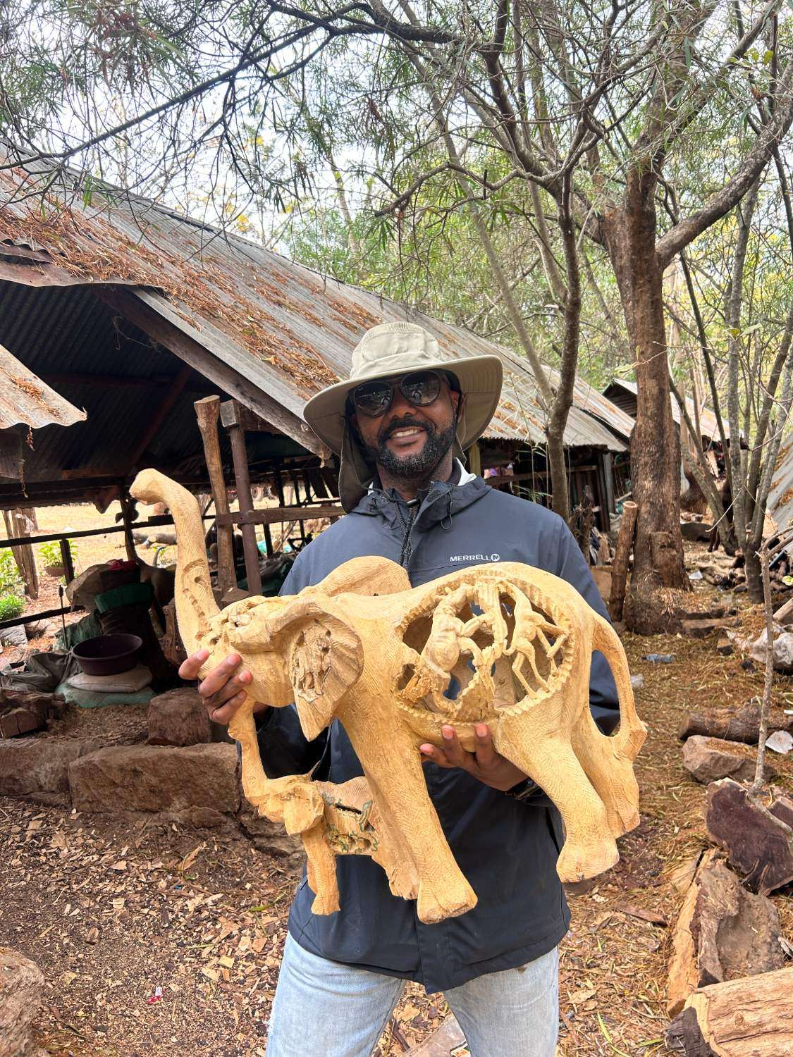 An elephant carving with animals cut through its flank, held in front of the sheds